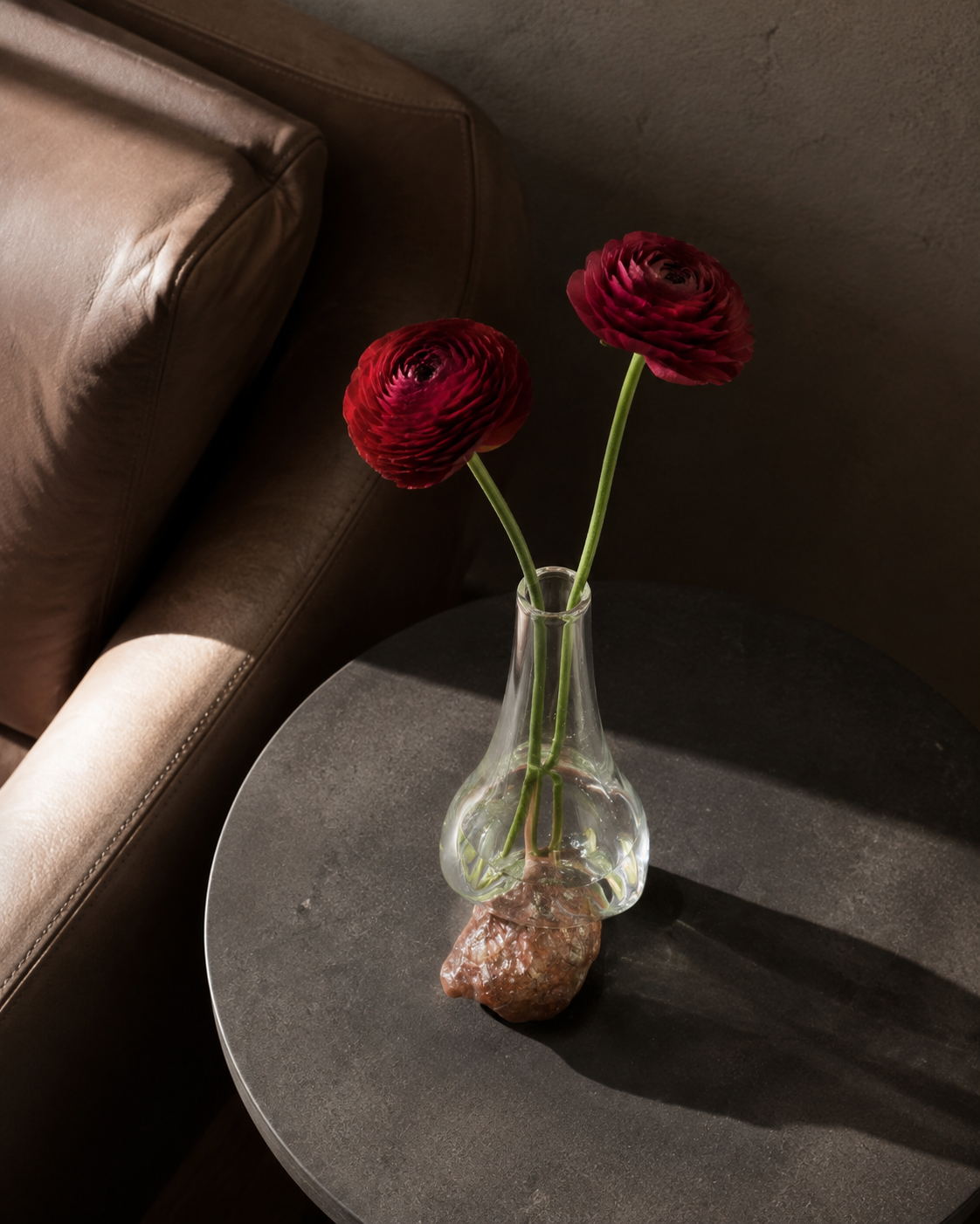 High-angle view of Stoneveil No. 006 styled with wine-red ranunculus in a leather lounge