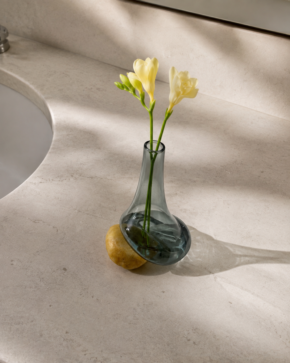 High-angle view of Stoneveil No. 003 styled with pale yellow freesia on a stone vanity