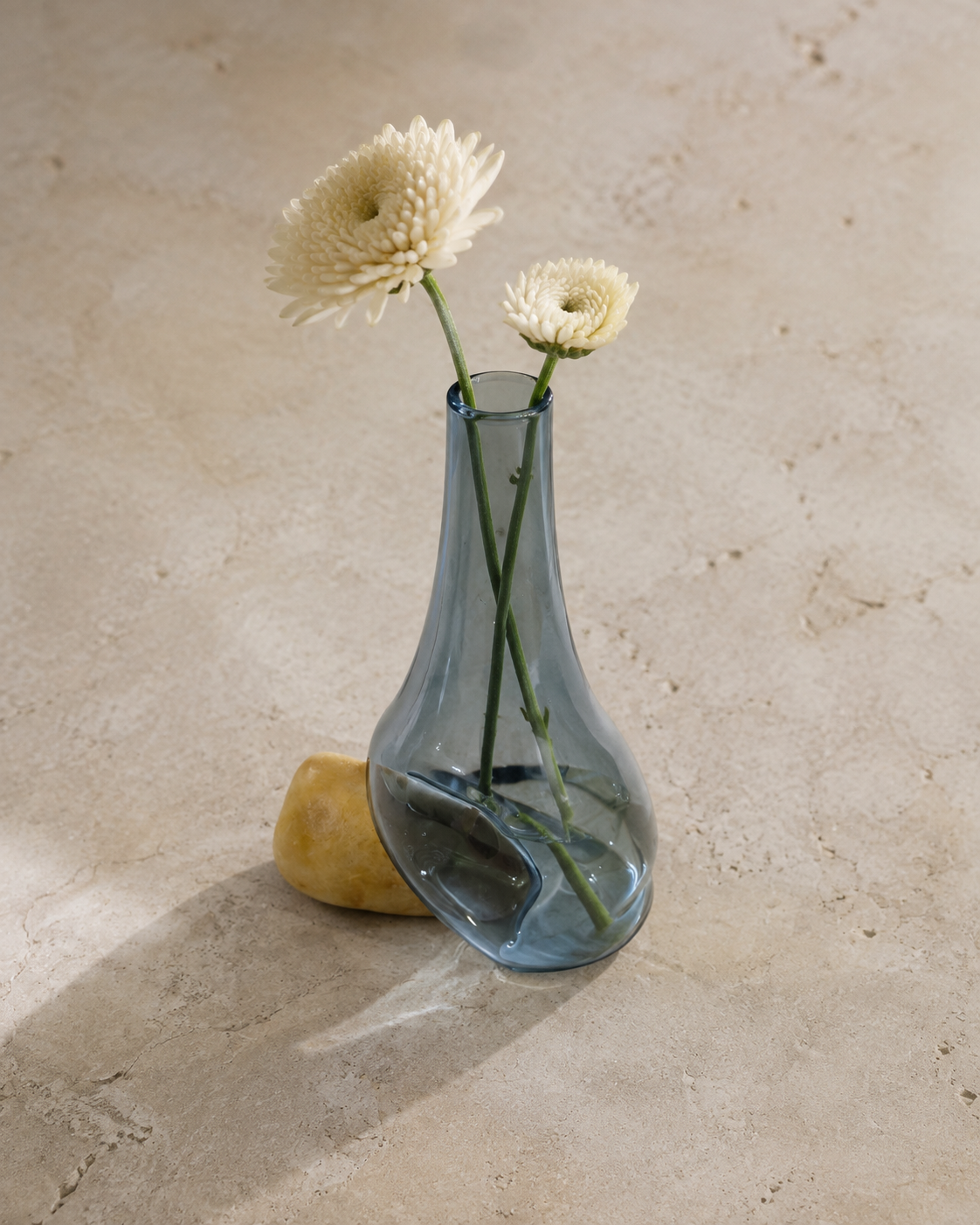 Stoneveil No. 007 gray-blue glass vase styled with cream chrysanthemums on a limestone tea table