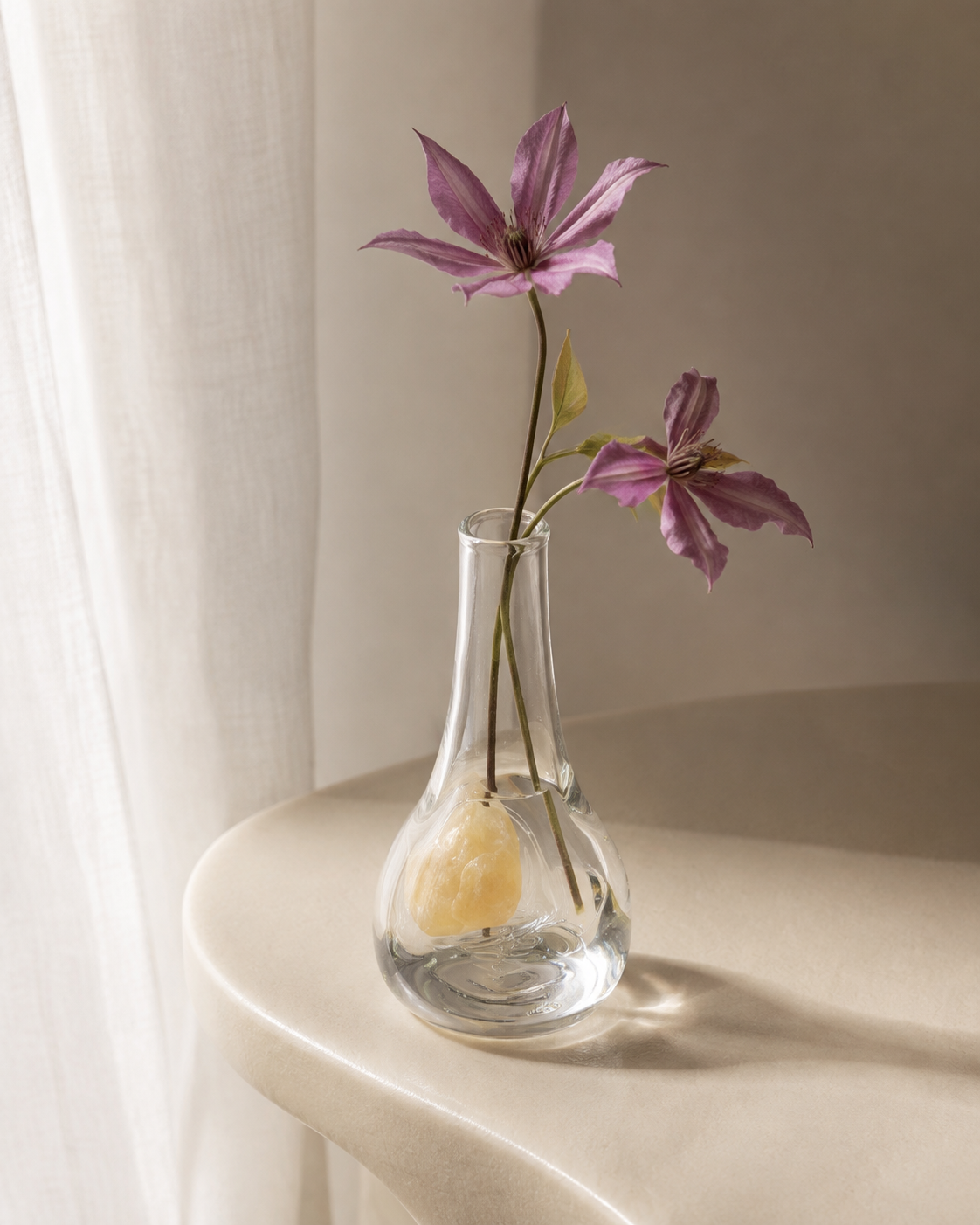Stoneveil No. 005 clear glass vase styled with mauve clematis on a curved side table